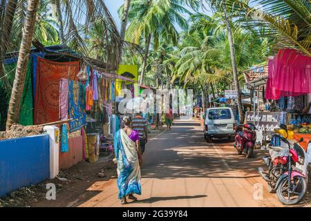 Femmina indiana in sari passeggiate lungo la colorata Agonda Beach Road, Agonda, Goa, India Foto Stock