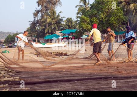 Pescatori indiani che tendono alla loro reti da pesca sulla spiaggia, Agonda, Goa, India Foto Stock