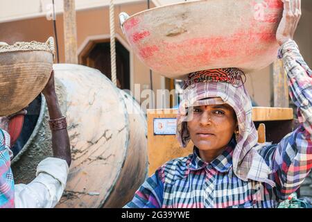 Lavoratrice manuale indiana femminile che trasporta il carico pesante sulla sua testa pone per la fotografia al luogo di costruzione, Agonda, Goa, India Foto Stock