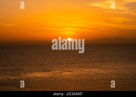 Tramonto arancione minimo sul Mar Rosso e sulle montagne sudanesi all'orizzonte, serata tranquilla, visto da una nave. Foto Stock