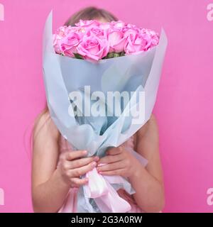 Una bambina in abito rosa con bouquet di rose, nascose dietro il flowers.The ragazza inala la fragranza di fiori su sfondo rosa Foto Stock