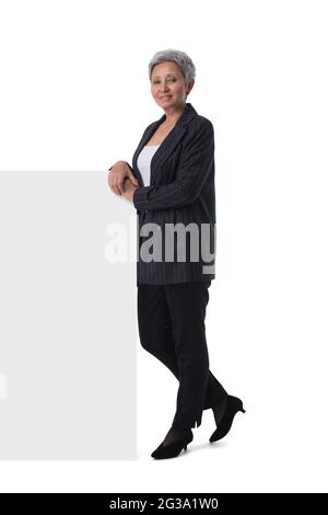 La donna asiatica matura sta tenendo una lavagna di testo vuota su sfondo bianco e mostrando il pollice in su Foto Stock