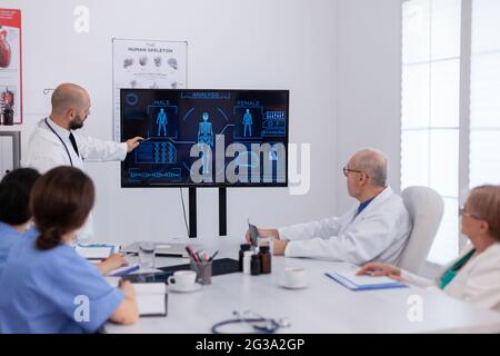 Medico uomo che presenta la radiografia del cervello che analizza la perizia medica che lavora nella sala riunioni della conferenza. Collaboratori neurologi che spiegano il trattamento di malattia indicando la presentazione sanitaria Foto Stock