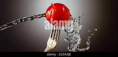 pomodoro di ciliegio su una forchetta d'argento, getto d'acqua, spray Foto Stock