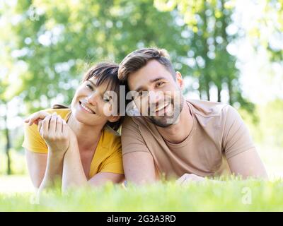 Felice coppia mid adult che giace all'aperto su erba e sorridente Foto Stock