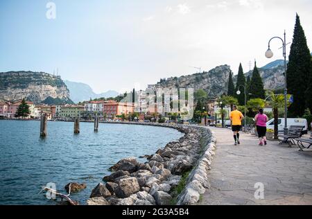 Nago Torbole, Italia. 14 Giugno 2021. Due joggers corrono lungo la passeggiata di fronte al paesaggio del porto. Monte Brione si vede sullo sfondo. Credit: Daniel Reinhardt/dpa/Alamy Live News Foto Stock