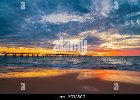 Onde che si infrangono alla spiaggia di Port Noarlunga con molo e tramonto spettacolare sullo sfondo Foto Stock