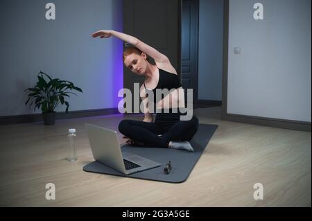 Durante l'auto-isolamento, la ragazza prende una lezione di yoga a casa, esegue esercizi di stretching. Foto Stock