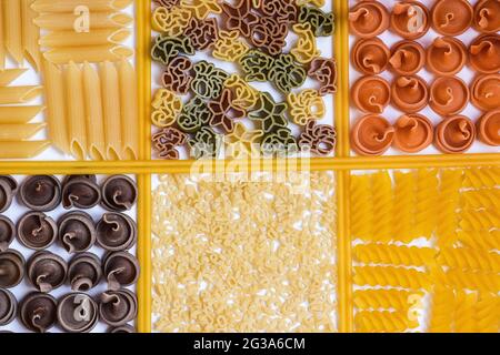 Pasta cruda e spaghetti di diversi colori e tipi sono disposti in celle quadrate. Foto Stock