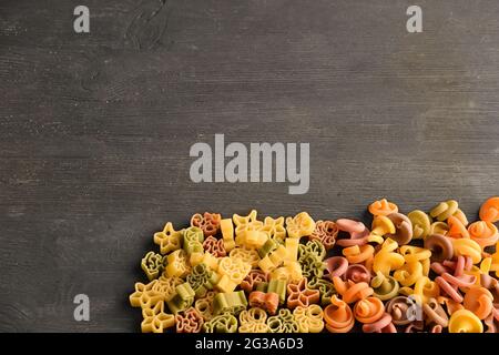 Pasta cruda di diversi colori e tipi, disposta su un tavolo scuro in legno. C'è molto spazio per il testo in alto Foto Stock