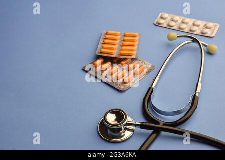 Stetoscopio e pillole diverse in vesciche su sfondo blu. A sinistra c'è un posto dove inserire testo o iscrizione Foto Stock