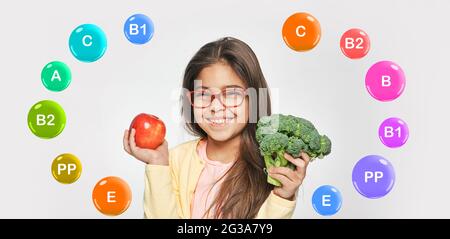 cibo vegetariano sano con vitamine per bambini. Sorridente ragazza mista che tiene in mano una mela e dei broccoli Foto Stock