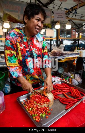 Un venditore tailandese di cibo di strada affetta una quantità abbondante di peperoni rossi, gialli e verdi da usare come ingrediente nel suo commercio di cibo da asporto. Foto Stock