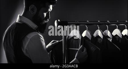 Abiti maschi appesi in fila. Abbigliamento da uomo, boutique. Su misura. Abito elegante da uomo. Costume da uomo, sarto nella sua officina. Bel bearded Foto Stock