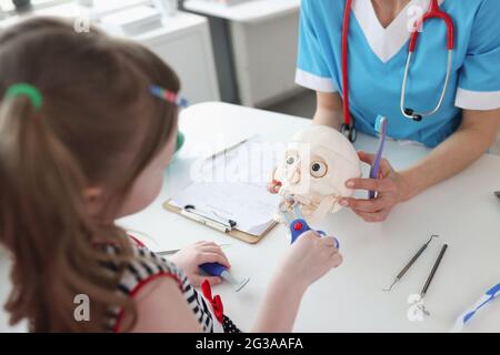 Bambina che tira fuori il dente con gli strumenti medici giocattolo sul cranio astronomico al closeup appuntamento dentista Foto Stock