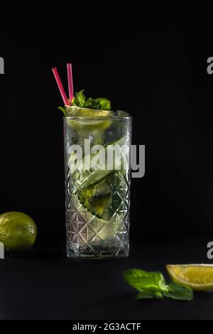 Limonata estiva fresca di cetrioli con due cannucce rosa nel bicchiere. Sfondo nero. Lime e menta sul tavolo. Foto Stock