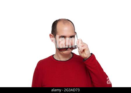 Un giovane calvo vestito con un maglione rosso che guarda in avanti mentre con la mano sinistra sta mettendo i suoi occhiali scuri davanti ai suoi occhi. Lo sfondo Foto Stock