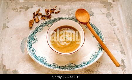 Zuppa di funghi fatta in casa con un vortice di panna in una ciotola bianca su un piatto vintage a motivi blu, con un cucchiaio di legno e porcini essiccati su una tovaglia rustica Foto Stock