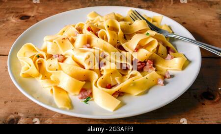 Tagliatelle Carbonara Italiana Pastina autentica su rustico sfondo in legno su piatto bianco con forchetta Foto Stock