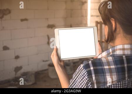 Una ragazza giovane sta progettando la costruzione e la ristrutturazione di un concetto di casa, mockup schermo tablet con bianco schermo in mano, copia spazio foto Foto Stock