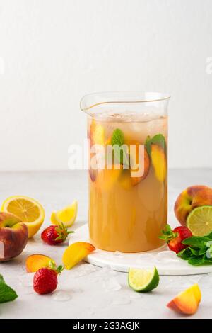 Succo fresco e rinfrescante con fette di pesca e menta con ghiaccio in una brocca da vicino, bevanda fredda estiva Foto Stock