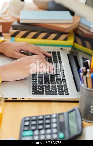 Primo piano di una ragazza irriconoscibile seduto al tavolo con una pila di notepad e calcolatrice e digitando sul computer portatile Foto Stock