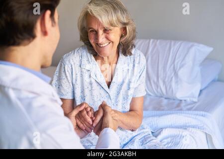 Il caregivista anziano tiene le mani di un anziano come consolazione nella casa di cura o nell'ospedale Foto Stock