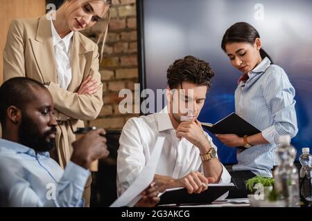 uomo d'affari attento che guarda il notebook vicino a colleghi multietnici Foto Stock