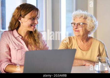Giovane donna e madre anziana insieme al tavolo usando un computer portatile a casa Foto Stock