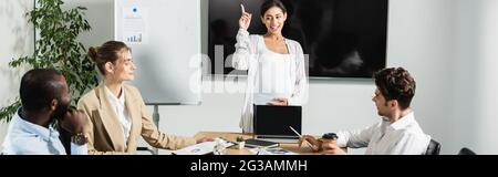 donna d'affari americana incinta che punta con il dito mentre parla con i soci d'affari, bandiera Foto Stock