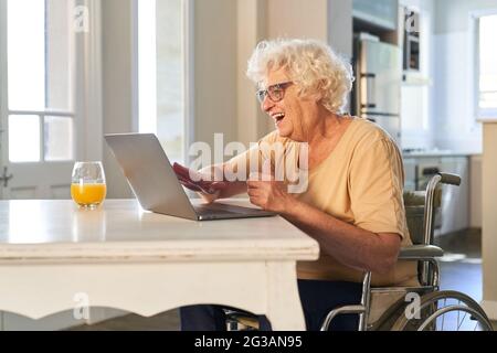 Donna anziana in sedia a rotelle che si gode di un computer portatile video chat con la famiglia a casa Foto Stock