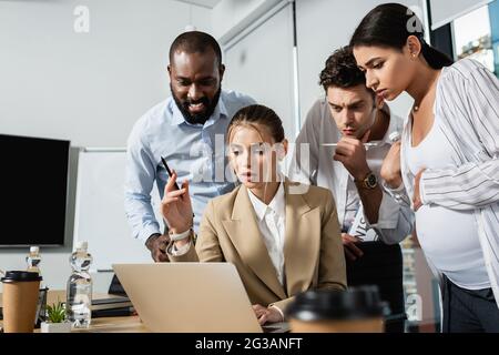 persone d'affari interrazziali sorprese e ponderate che guardano il notebook durante la riunione Foto Stock