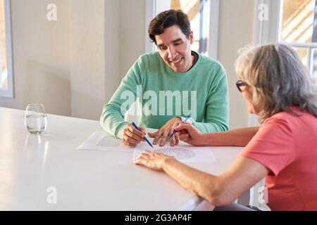 Giovane uomo e madre anziana con demenza risolvere puzzle labirinto come formazione di memoria Foto Stock