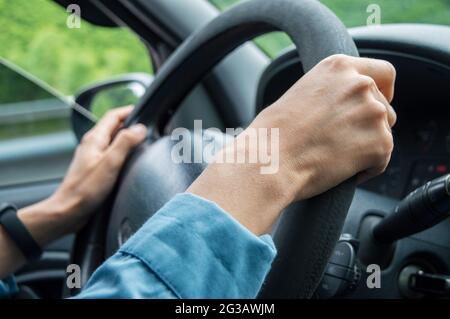 una giovane donna sta tenendo il volante con le mani. la donna sta guidando nel traffico. Foto Stock