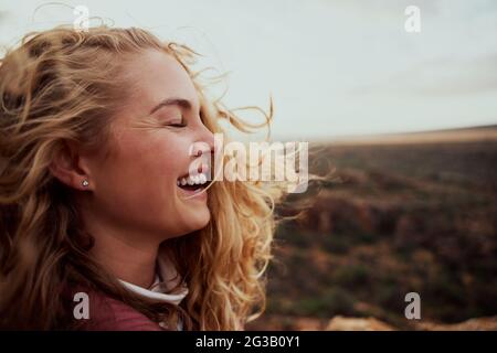 Vista laterale di bella giovane donna sensazione di vento brezza che tocca faccia con i capelli che volano Foto Stock