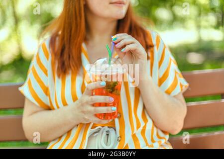 Estate bella donna felice mani tenere rinfrescante aperol spritz cocktail al parco della città. Concetto di cibo sano Foto Stock