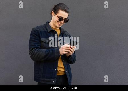 Jolly giovane uomo bearded usando i gadget all'aperto Foto Stock