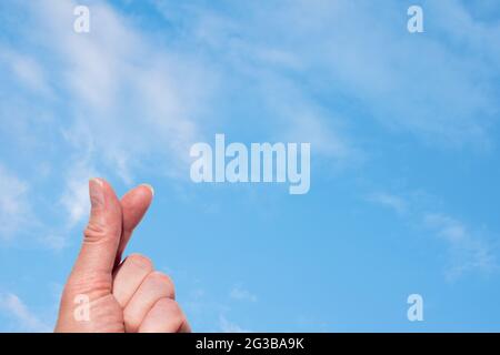 Una mano che forma un cuore con due dita sullo sfondo di un cielo blu con nuvole bianche e soffici. Simbolo coreano dell'amore con le dita. Dito Foto Stock