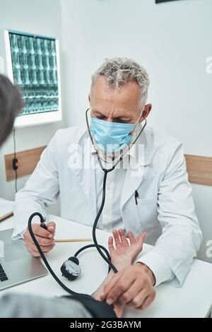 Medico concentrato che misura la tensione sanguigna del paziente Foto Stock