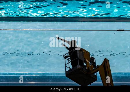 Londra, Regno Unito. 15 giugno 2021. I pulitori delle finestre vengono a lavare l'esterno usando un picker di ciliegia - Embassy Gardens, Nine Elms, residenti e i loro ospiti godono di accesso esclusivo alla Sky Pool sotto il sole. La piscina trasparente lunga 25 metri è realizzata interamente in acrilico e si estende tra i tetti degli edifici Legacy. Credit: Guy Bell/Alamy Live News Foto Stock