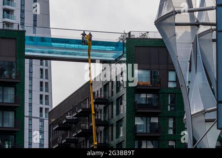 Londra, Regno Unito. 15 giugno 2021. I pulitori delle finestre vengono a lavare l'esterno usando un picker di ciliegia - Embassy Gardens, Nine Elms, residenti e i loro ospiti godono di accesso esclusivo alla Sky Pool sotto il sole. La piscina trasparente lunga 25 metri è realizzata interamente in acrilico e si estende tra i tetti degli edifici Legacy. Credit: Guy Bell/Alamy Live News Foto Stock