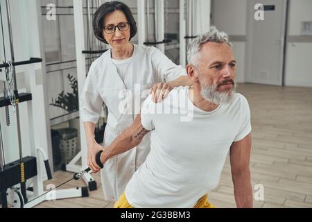 Atleta maschile che lavora sotto la supervisione di un esperto cinesiologo Foto Stock