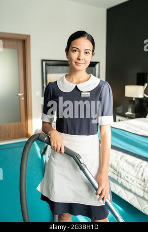 Bellissima cameriera con aspirapolvere che ti guarda Foto Stock