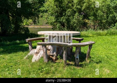 Un tavolo composto da un tronco d'albero con un piano in cemento e posti a sedere in legno in piedi su un prato vicino al fiume. Foto Stock