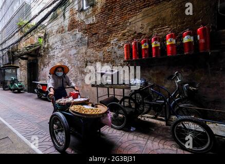 Un'anziana venditrice di strada femminile, che vende noci, spinge il suo carrello lungo un vicolo stretto, poco illuminato, Chinatown, Bangkok, Thailandia Foto Stock