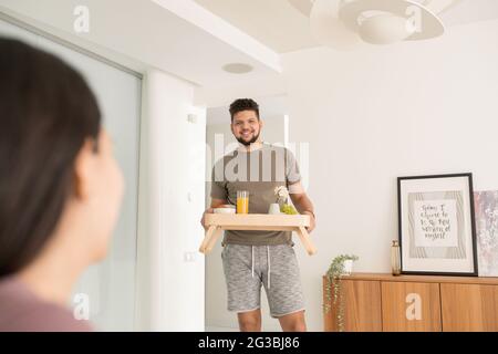 Felice giovane uomo che porta il vassoio con la colazione per sua moglie Foto Stock