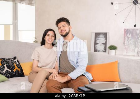 Affettuosa coppia seduta sul divano mentre si riposa in ambiente domestico Foto Stock