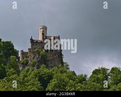 Splendida vista ad angolo basso del popolare castello di Lichtenstein situato sulla scarpata dell'Alb Svevo, Germania con foresta verde in primavera e cielo nuvoloso. Foto Stock