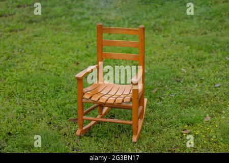 una piccola sedia dondolante di legno per bambini che si siede fuori da sola sull'erba Foto Stock