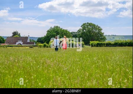 Un gruppo di rambler che camminano su un campo di erba alta con i Downs del sud che si innalzano in lontananza nel Sussex orientale, Inghilterra. Foto Stock